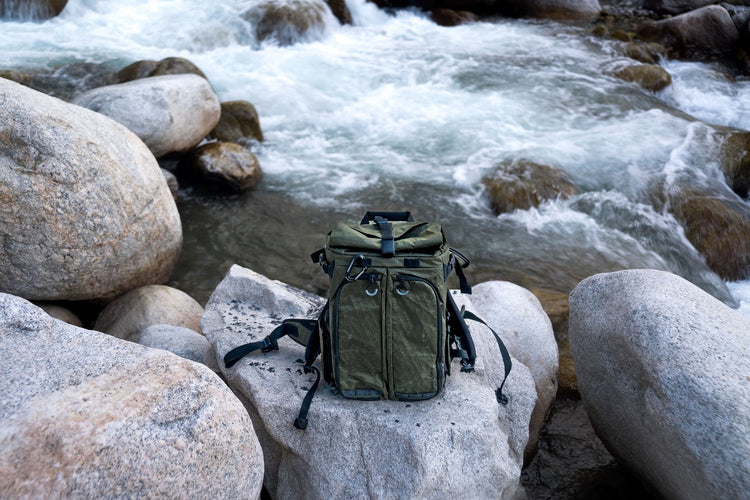 Green Gura Gear Kiboko camera backpack on a boulder beside a mountain river