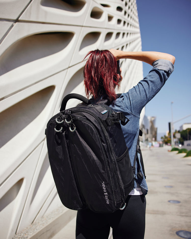 A woman with red hair wearing a black Kiboko 2.0 16L+ beside a sculpted white wall