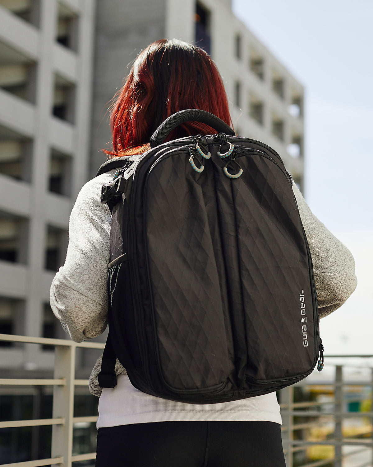 A woman with red hair wearing a black Kiboko 2.0 16L+, seen from behind in the city