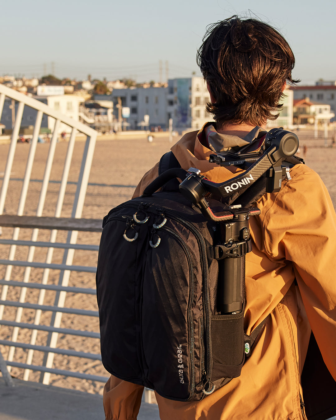 A person in an orange jacket wearing a black Kiboko 2.0 16L+ with a gimbal strapped to the side