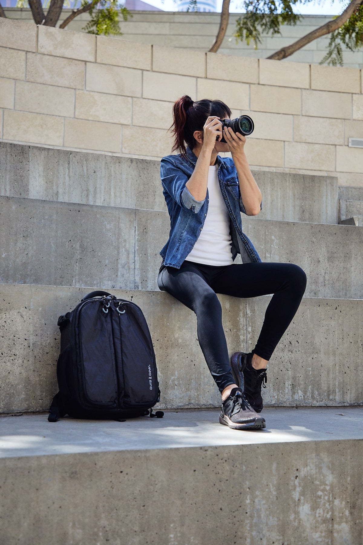 A woman photographing from concrete steps with a black Kiboko 2.0 22L+ beside her