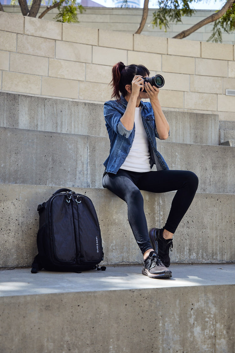 A woman photographing from concrete steps with a black Kiboko 2.0 22L+ beside her