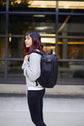 A woman wearing a black Kiboko 2.0 22L+ on her back, side view in front of a glass building