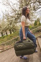 A woman carrying a Forest Green Kiboko 2.0 30L+ by its top handle up outdoor stairs